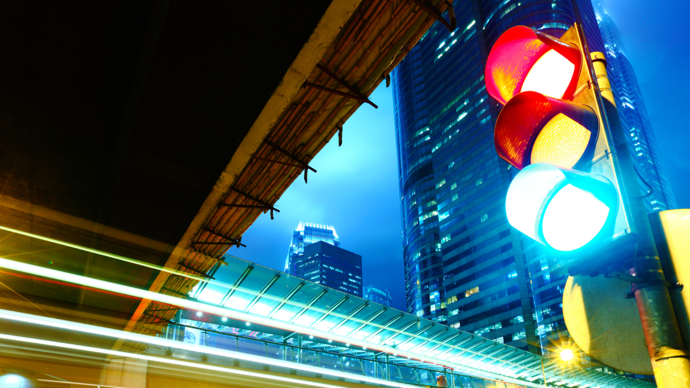 Dettaglio fotografico di un semaforo intelligente dotato di sensori iot in un incrocio cittadino al tramonto.